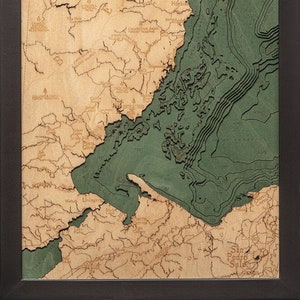 May include: A wooden map of Belize with a compass rose in the upper left corner. The map is framed in black and shows the coastline and rivers of Belize. The ocean is shown in green.