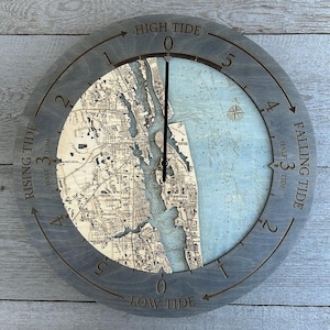 May include: A circular tide clock featuring a map of St. Augustine, Florida. The clock face is marked with tide phases, including "High Tide" and "Low Tide." The hands indicate the current tidal stage. The clock is grey.