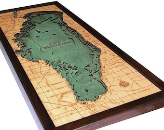 Pode incluir: Um mapa de parede retangular de madeira do lago Winnebago com um design tridimensional em camadas. O lago é representado com um acabamento verde texturizado e curvas de nível, rodeado por madeira clara com estradas gravadas.