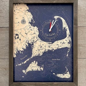 May include: A rectangular wall clock featuring a nautical map of Cape Cod Bay, Buzzards Bay, and Nantucket Sound. The map has a light wood-toned landmass against a deep blue ocean background, encased in a dark gray wooden frame.