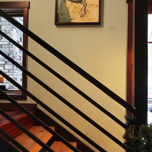 K&ouml;nnte beinhalten: Eine Holzkarte der Salish Sea h&auml;ngt an einer Wand mit einem Holzrahmen. Die Karte ist hellbraun mit blauen Wassermerkmalen. Die Karte h&auml;ngt an einer Wand mit einer Holztreppe im Vordergrund.