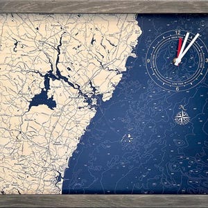 May include: A rectangular wall clock featuring a nautical map of the Portsmouth coastline. The left side shows land in light beige, while the right side depicts deep blue ocean depths. It includes a tide clock face, a compass rose, and a gray frame.