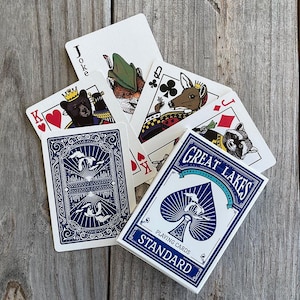 May include: A deck of Great Lakes playing cards with a blue and white box featuring a spade logo. The cards display illustrations of animals including a bear, a fox, a deer, and a raccoon, with the text Great Lakes Standard on the box front.