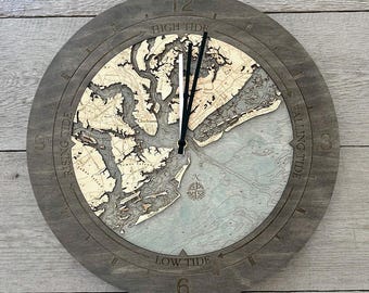 以下が含まれることがあります： チャールストン海岸線の詳細な水深図が描かれた木製の丸い掛け時計。ダークグレーのフレームには、High Tide、Rising Tide、Low Tide、Falling Tideの文字が刻まれています。黒い時針と分針が付いています。