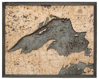 May include: A framed wooden bathymetric map of Lake Superior featuring layered blue-grey water depths set against a light tan landmass. The map includes engraved labels for Minnesota, Ontario, Michigan, and Wisconsin with a compass rose.