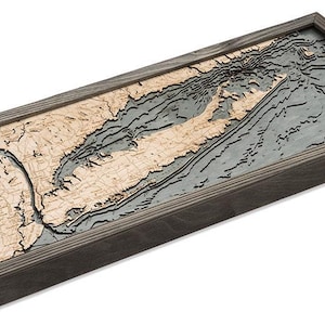 May include: A rectangular wooden wall art piece featuring a 3D bathymetric map of a coastline. The land is represented by light-colored wood layers, while the water is depicted in dark gray, all encased within a dark stained wooden frame.