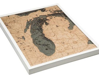 May include: A three-dimensional wooden bathymetric map of Lake Michigan encased in a white frame. The map features layered tan landmasses with engraved roads and cities, contrasting with the deep, recessed gray water depths.