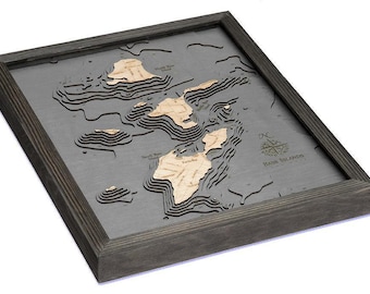 May include: A framed 3D bathymetric wood map of the Bass Islands featuring layered light-colored wood islands set against a dark gray water background. The map includes a compass rose and the text Bass Islands printed on the surface.
