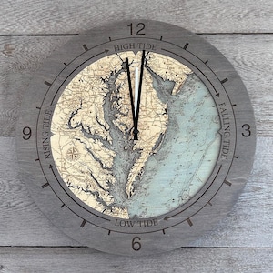May include: A circular wall clock with a gray wooden frame featuring a nautical map of the Chesapeake Bay region. The clock face displays the numbers 3, 6, 9, and 12, with text indicating High Tide, Falling Tide, Low Tide, and Rising Tide.