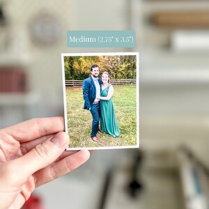Pu&ograve; includere: Una fotografia rettangolare che ritrae una persona in abito blu navy e una persona in abito verde in piedi in un campo erboso con una staccionata in legno sullo sfondo. Il testo Medium (2,75" x 3,5") &egrave; presente in alto.