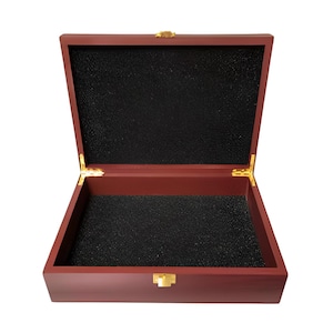 May include: Open, rectangular wooden box with a dark red finish. The interior is lined with black foam. The box has gold-colored hinges and a gold-colored clasp. The lid is open, revealing the interior.