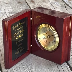 May include: A mahogany book-shaped clock with a gold-colored face and hands. The clock has a plaque on the front that reads "Bonnie Francis Thank You for 30 Years of service to the Quincy Public Library."