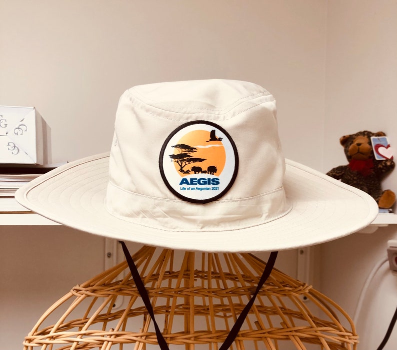 May include: A white safari hat with a brown brim and a blue and white logo that says "AEGIS Life of an Aegonian 2021" with a silhouette of a bird and animals in a savanna setting.