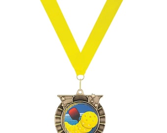May include: A gold-colored medal with a yellow ribbon. The medal features a colorful image of a pickleball paddle and ball in a net. The medal has a star-shaped design around the edge.