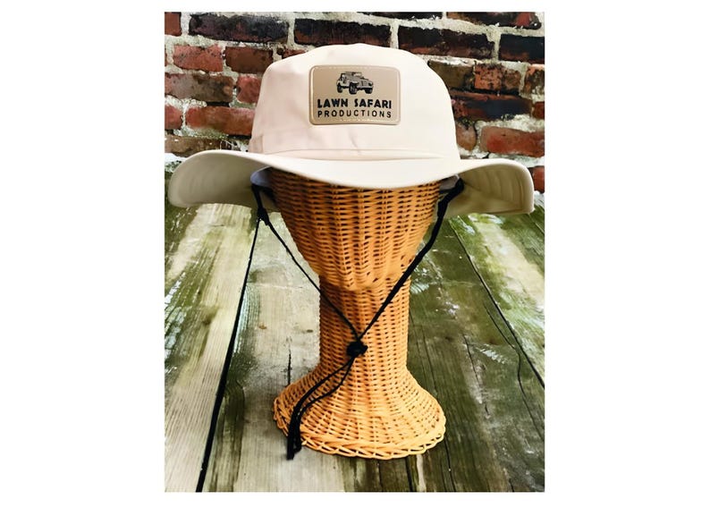 May include: A beige sun hat with a black chin strap and a brown patch with the text "LAWN SAFARI PRODUCTIONS" and a small image of a jeep.