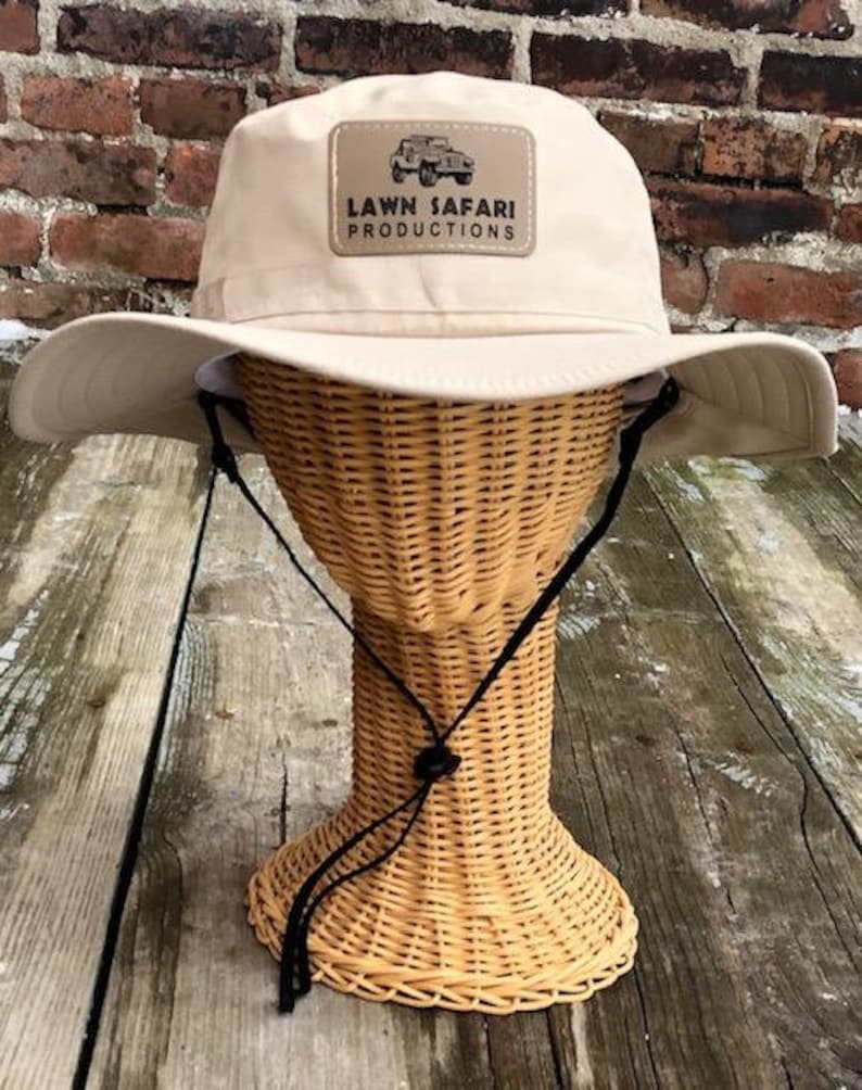 May include: A beige sun hat with a brown patch that says "LAWN SAFARI PRODUCTIONS" and a picture of a jeep.