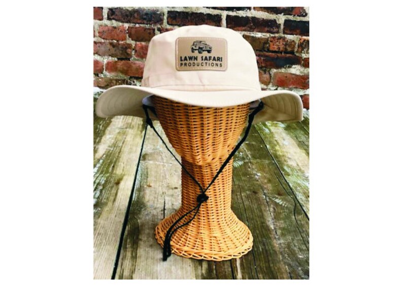 May include: A beige canvas bucket hat with a brown patch on the front that says "LAWN SAFARI PRODUCTIONS" with a small image of a jeep.