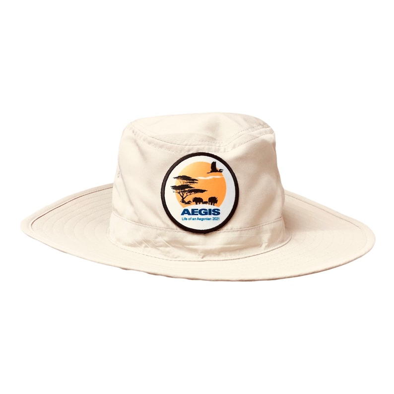 May include: A beige safari hat with a round patch featuring a sunset scene with a bird flying over a savanna with trees and elephants. The patch has the text "AEGIS Life of an Aeginian 2021" in blue and black.