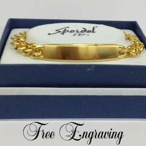 May include: Gold-toned Speidel ID bracelet with a flat, rectangular tag. The bracelet is in a blue box with a white interior and the words "Free Engraving" printed on the bottom.