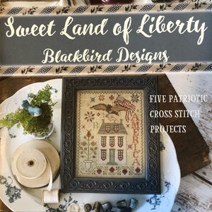 May include: A collection of patriotic cross-stitch projects, including a framed sampler with an American flag and eagle design. The image features the text "Sweet Land of Liberty" and "Blackbird Designs."