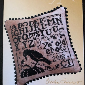 May include: A cross stitch sampler pattern featuring the alphabet, a crow, and the text "Ye old crow, 2018". The pattern is from Heart in Hand Needleart.