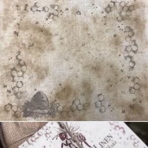 May include: A white tag with brown text that reads "Prim Bee Linen by The Primitive Hare 30ct Linen". The tag is on a brown burlap fabric with a white flower and a bee illustration.