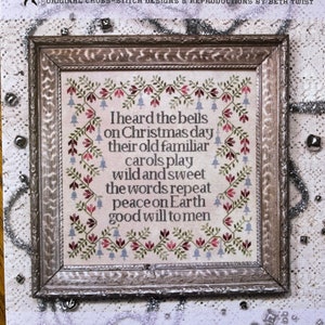 May include: A framed cross-stitch sampler with the text "I heard the bells on Christmas day..." surrounded by floral and bell motifs. The sampler is in a decorative wooden frame, with the words "Christmas Bells Sampler" at the bottom.