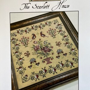 May include: A framed cross-stitch pattern with a floral design and birds. The title of the pattern is "The Scarlett House Roses For Ruby".