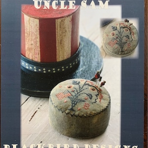 May include: A cross stitch pattern for a pincushion featuring a red, white, and blue floral design with the text "Hats Off to Uncle Sam" and "Blackbird Designs".