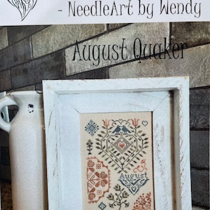 May include: A framed cross-stitch pattern with a white background and a colorful design featuring birds, flowers, and the word "August". The frame is white with a distressed finish. The title "From the Heart - Needle Art by Wendy August Quaker" is visible above the frame.