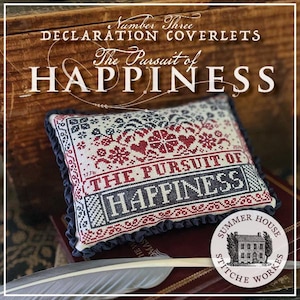 May include: A rectangular cross-stitch pillow featuring red and dark blue embroidery on a cream fabric. The text reads THE PURSUIT OF HAPPINESS, 1776, and includes decorative heart and floral motifs. The pillow is finished with a dark blue ruffled trim.