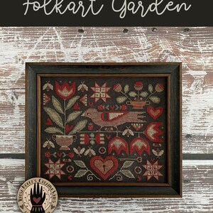 May include: Folkart Garden cross stitch pattern featuring a bird, flowers, hearts, and a key. The pattern is framed in a dark wood frame and has a black background.