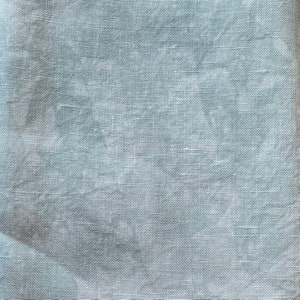 May include: Close-up of a light blue linen fabric. The fabric has a fine, woven texture with subtle variations in color and tone. The material appears soft and slightly wrinkled, suggesting a natural fiber.