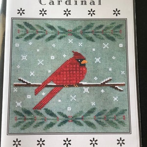 May include: A cross-stitch pattern titled "Wintertide Cardinal" showing a red cardinal on a branch, with green sprigs and snowflakes on a teal background. The text "Make A Festive Holiday Pillow" is also visible.