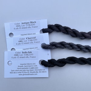 May include: Three spools of black silk thread for embroidery. The spools are labeled with the color, lot number, and length of thread. The colors are Antique Black, Charcoal, and India Ink.