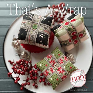 May include: Three small, square, fabric-covered cushions with a Christmas theme. The cushions are decorated with red, green and white fabric and have a button in the centre. The cushions are on a white plate with a green background.