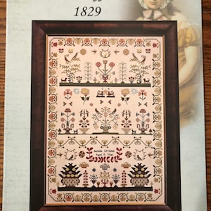 May include: A framed cross-stitch sampler with a floral design and the text "Isabella Uffindell Aged 10 Years". The sampler is in a brown frame with a gold trim. The image is from the "Hands Across the Sea Samplers" collection.