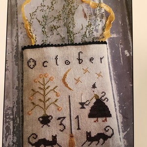 May include: A beige fabric bag with black stitching and a black scalloped border. The bag features an embroidered design of a witch, a cauldron, a broom, a crescent moon, a black cat, and the text "October 31".