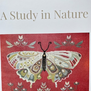 May include: A cross-stitch pattern featuring a colorful butterfly with intricate details, surrounded by small white flowers on a red background. The title "A Study in Nature" is displayed above the design. The text "The Artsy Housewife" is displayed in a banner above the title.