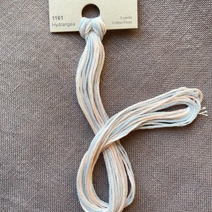 May include: A skein of Weeks Dye Works floss in the color Hydrangea, a light blue and cream color. The floss is 5 yards long and is made of cotton.