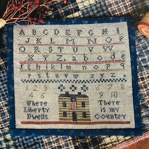 May include: Cross-stitch sampler with a house, flowers, and the text "Where Liberty Dwells" and "There is my Country". The sampler also includes the alphabet and numbers.