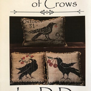 May include: Three cross-stitch pillow designs featuring black crows. The top pillow has a crow with a red berry in its beak and the text "October 31". The bottom two pillows each feature a crow with a branch of red berries. The text "La-D-Da designs for counted thread" is at the bottom of the image.