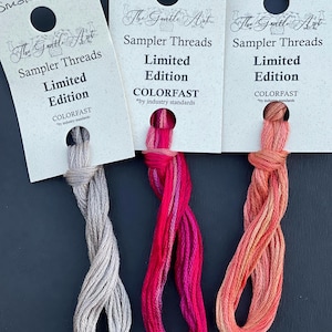 May include: Three sampler threads in shades of gray, pink, and orange. Each thread is attached to a card with the text "The Gentle Art Sampler Threads Limited Edition COLORFAST". The cards are labeled "Smokeshow", "VAVA VOOM", and "Showgirl".