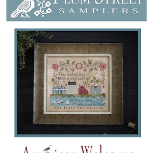 May include: Framed cross-stitch sampler with the text "This land we love so vast and free" and "We honor those who cared for thee." The sampler features houses, sailboats, and an American flag. The words "American Welcome" are below the sampler.