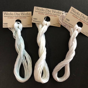 May include: Three spools of Weeks Dye Works floss in white, white with a hint of blue, and a light blue. Each spool has a label with the brand name, floss collection, color number, and color name. The spools are 5 yards each.