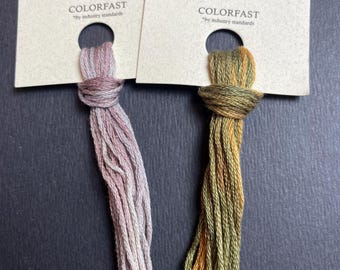 May include: Two skeins of embroidery floss, one is a light pink and the other is a green and brown blend. The skeins are labeled "The Gentle Art Sampler Threads Limited Edition" and "COLORFAST by industry standards".