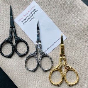 May include: Three pairs of antique-style scissors with rose details on the handles. The scissors are black, silver, and gold.
