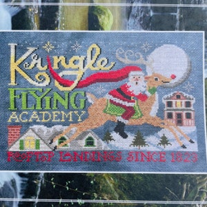 May include: A cross-stitch pattern featuring Santa Claus flying on a reindeer with the text "Kringle Flying Academy Rooftop Landings Since 1823".