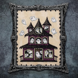 May include: Cross-stitch of a haunted house with ghosts in the windows and floating around it. The house is purple and black, with a black roof and a porch. The artwork is framed in a decorative silver frame.