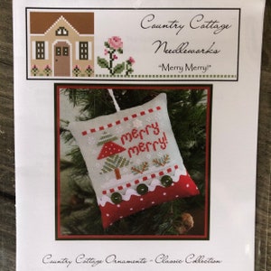 May include: A cross-stitch pattern for a Christmas ornament featuring a small tree with a red mushroom and the text "Merry Merry!" The ornament is white with red and green accents and a red and white polka dot trim.